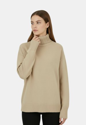 Maglione a collo alto beige con polsini e orlo a costine. Tessuto liscio, vestibilità comoda e design sobrio. Indossato sopra un capo nero.