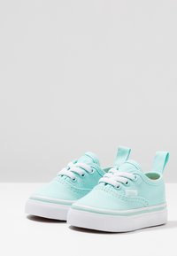 Vaaleansiniset kangaskengät, joissa on valkoiset nauhat, kumipohja ja silmukkamainen kantatuki. Ominaisuuksia ovat kontrastiväriset ompeleet ja hillitty logo sivussa.