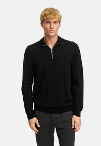 Zwarte pullover trui met een kwart rits, gebreide structuur, lange mouwen en geribde manchetten en onderkant. Draag over donkergrijze broek.