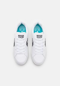 Adidași albi cu accente negre, având un upper din piele netedă, vârf rotund, design cu șireturi și o talpă interioară turcoaz cu un model circular.