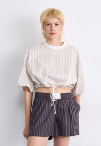 Top corto a maniche corte a righe beige e crema, con orlo regolabile, abbinato a pantaloni corti a righe scure con vita elasticizzata.