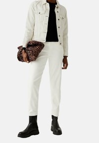 Witte denimjas, zwart topje, witte broek en zwarte chunky enkellaarsjes. Houdt een bruin tasje met luipaardprint vast.