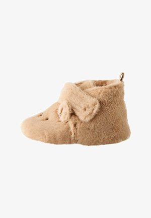 Pantofole morbide beige pelose con copertura alla caviglia e cinturino regolabile su sfondo bianco semplice.