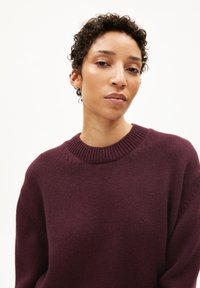 Burgunderfarbener Strickpullover mit einem gerippten Rundhalsausschnitt, lässiger Passform, strukturiertem Stoff und subtilen Nähdetails an den Ärmeln.