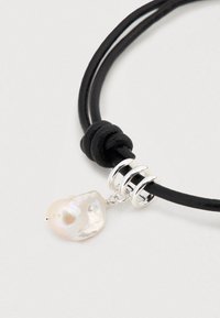 Μαύρο δερμάτινο κολιέ με κόμπο και ασημένιες λεπτομέρειες. Ένα μόνo ασύμμετρο λευκό μαργαριτάρι κρεμαστό προσθέτει μια μοναδική πινελιά.