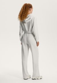 Šedá mikina s kapucňou a zodpovedajúce tepláky vyrobené z mäkkého materiálu. Mikina má šnúrku na stiahnutie a tepláky majú elastický pás a rovné nohavice.