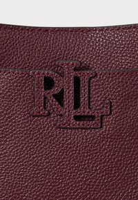 Burgundijas ādas soma ar teksturētu virsmu, kurai ir melns "RL" logotips. Šuvju malas un gluda, smalka spīduma klātbūtne uzlabo dizainu.