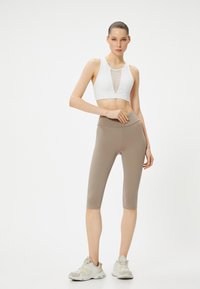 Top deportivo blanco recortado con detalle de malla, combinado con leggings de talle alto en color beige. Llevado con zapatillas deportivas de colores claros.