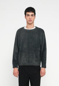 Tmavosivý mäkký sveter s širokým výstrihom, dlhými rukávmi a voľným strihom, kombinovaný s čiernymi nohavicami. Jemná textúra a minimalistický dizajn.