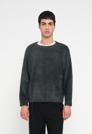 Tumehall fliisist kampsun lai kaelusega, pikkade varrukatega ja lõdva istumisega, mida on kombineeritud mustade pükstega. Pehme tekstuur ja minimalistlik disain.