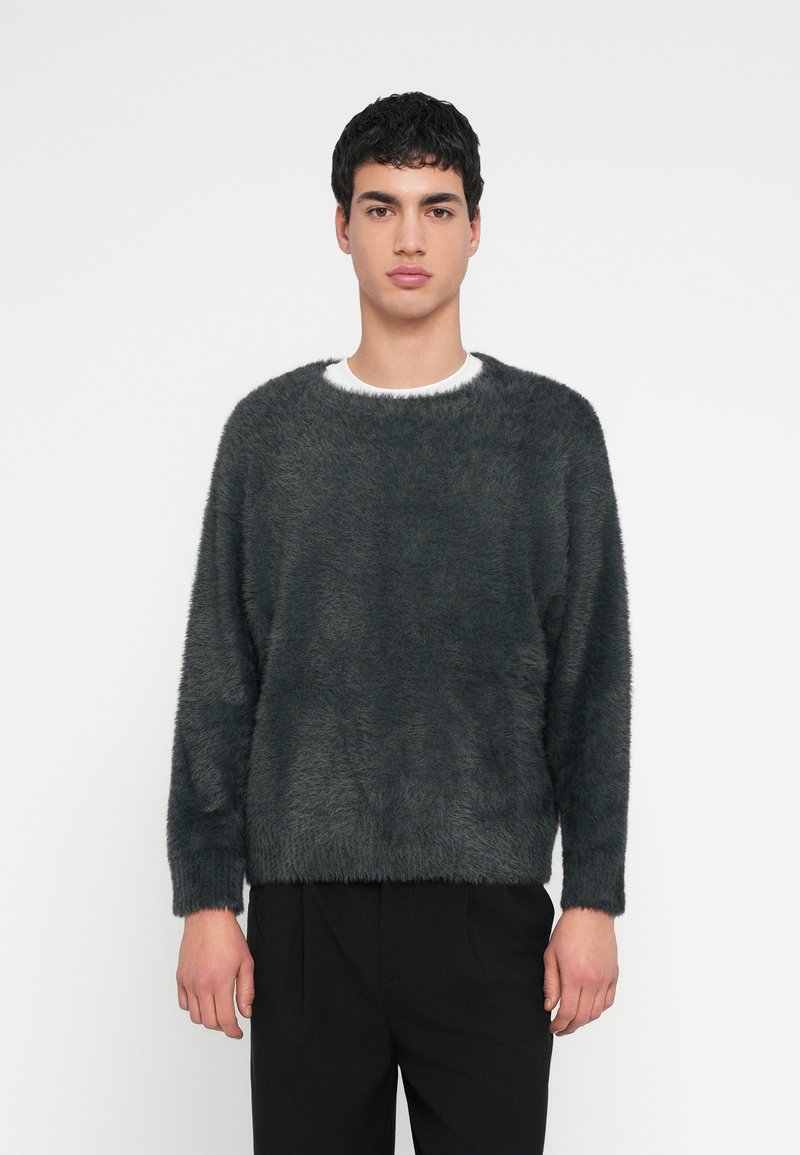 Tmavosivý mäkký sveter s širokým výstrihom, dlhými rukávmi a voľným strihom, kombinovaný s čiernymi nohavicami. Jemná textúra a minimalistický dizajn.