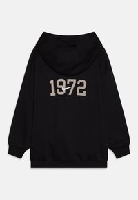 Melna kapuce ar lielu bēšas krāsas "1972" apdruku aizmugurē, kas ietver baltu Nike zīmolu. Izgatavota no mīksta, strukturēta auduma.