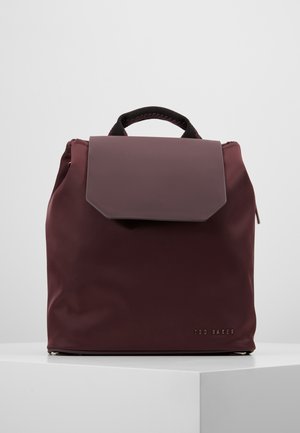 Donkerpaarse rechthoekige rugzak met bovenhandvat, klepsluiting en een klein "Ted Baker" logo aan de voorkant, getoond op een witte ondergrond.