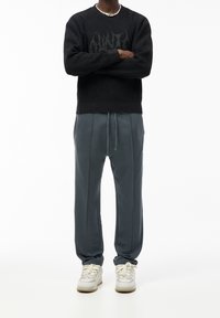 Svart stickad tröja med ribbat mönster och grafisk design, som kombineras med gråa tapered sweatpants och vita sneakers.