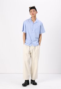 Chemise à rayures à manches courtes en bleu clair, avec un col à encolure et une poche sur la poitrine. Associée à un pantalon à large jambe couleur crème et des bottes noires.