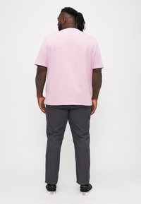 Tricou din bumbac roz deschis, cu mâneci scurte, asociat cu pantaloni cargo gri închis, cu buzunare laterale. Purtați cu pantofi negri.