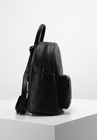 Mochila de cuero negra texturizada con forma redondeada, que cuenta con un cierre de cremallera, bolsillo lateral y correa ajustable. Material suave y duradero.