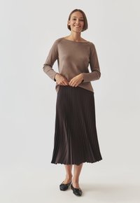 Haut marron à manches longues associé à une jupe midi plissée marron foncé et à des chaussures plates noires, mettant en avant une texture lisse et une coupe décontractée.