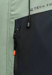 Light green and black jacket section featuring a zipper, adjustable drawcord, and a logo printed in black. Smooth fabric with a matte finish.