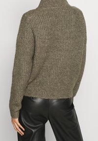 Pull en maille vert olive avec un col haut, doté d'une finition texturée et d'un ourlet côtelé. Associé à un pantalon en cuir noir élégant.