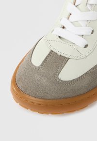 Baskets avec une tige en daim gris et cuir crème, lacets blancs, et une semelle en caoutchouc marron. Caractérisées par des détails cousus et une forme de bout arrondi.