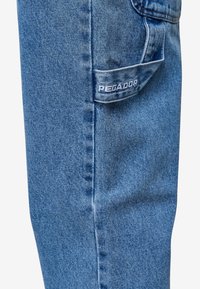 Světle modré denimové džíny se slim fit, s viditelnou zadní kapsou označenou "PEGADOR" bílým šitím. Hladká, mírně texturovaná tkanina.
