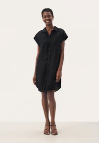 Abito camicia corto nero a maniche corte con chiusura a bottoni frontale, due tasche sul petto e vestibilità comoda, realizzato in tessuto leggero.
