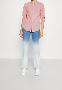 Red and white striped shirt with a button-down collar, paired with light blue gradient flared jeans. White sneakers complete the outfit.