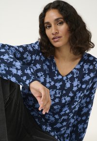 Navyblouse met lichtblauw bloemetjespatroon, V-hals, lange mouwen en knopenmanchetten. Zacht materiaal met een relaxte pasvorm.