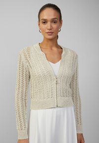 Licht beige gebreide cardigan met een rits aan de voorkant, kenmerken een gestructureerd, open geweven ontwerp en geribde manchetten en zoom.