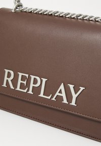 Borsa a tracolla in ecopelle marrone con catena argentata, grande logo impresso "REPLAY" e texture liscia con dettagli di cucitura discreti.