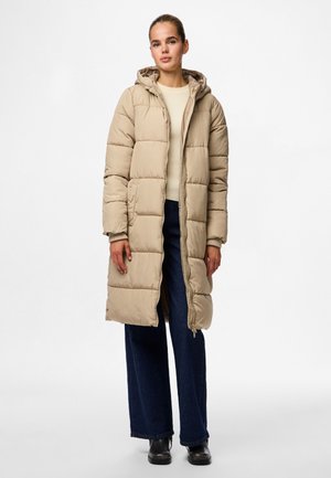 Beige lang pufferjakke med hette, quiltet design, frontglidelås og sidelommer. Kombinert med en lys genser og vide, mørke jeans.