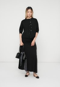 Μαύρος ζακέτας με χρυσά κουμπιά, μαύρο εφαρμοστό φόρεμα, μαύρες μπαλαρίνες με αντίθετο καπάκι, και μαύρη τσάντα χειρός με φουλάρι με πουά.