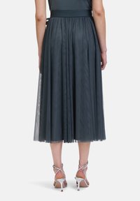 Jupe en tulle teal à plusieurs niveaux avec une taille ajustée, présentant un design plissé, une texture superposée et une finition transparente, assortie de talons argentés.