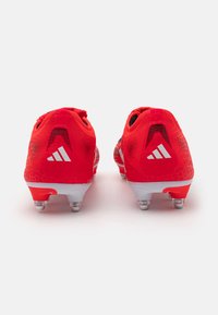 Red soccer cleats with a textured pattern, featuring white logo accents, and a lightweight design. Equipped with white studded soles for traction.