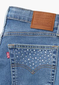 Jeans de ganga azuis com um remendo de pele nas costas com marcação em relevo e um bolso traseiro adornado com tachas prateadas.