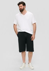 Witte V-hals t-shirt en zwarte knie-lange shorts, gecombineerd met witte sneakers. Glad materiaal, losse pasvorm, geen zichtbare patronen of accenten.