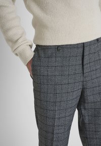 Grijze geblokte broek met een gestructureerde stof, voorzien van een getailleerde pasvorm en zijzakken, gecombineerd met een crèmekleurige ribbeltrui.