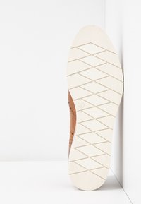Chaussure en cuir marron avec une surface texturée, présentant des détails perforés et une semelle en caoutchouc avec un motif de marche en zigzag. Taille 37.