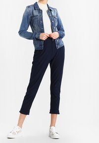 Chaqueta de mezclilla con un degradado azul claro; ajustada, con cierre de botones al frente. Top de punto acanalado blanco debajo. Pantalones cortos azul marino y zapatillas blancas.