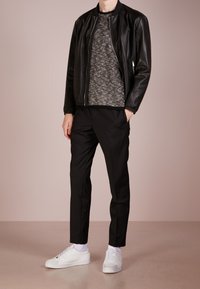 Veste bomber en cuir noir sur un pull texturé gris, associée à un pantalon noir et des baskets blanches. Tenue simple et décontractée.