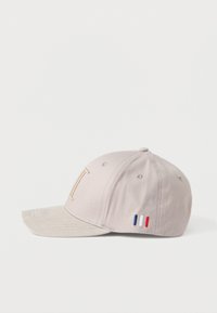 Világosszürke sapka bézs árnyalatú napellenzővel, arany betűkkel és egy kis piros, fehér, kék francia zászló jelvénnyel az oldalon.