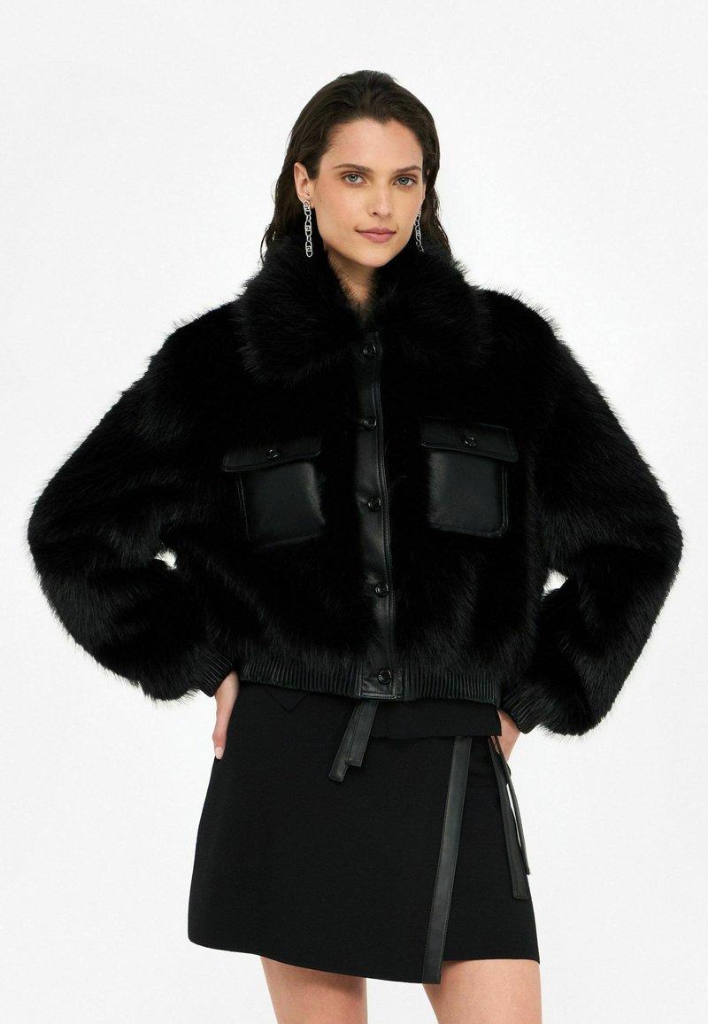 Veste bomber en fausse fourrure noire avec un devant et un col en cuir, dotée de deux poches avant, de poignets côtelés et d'un ourlet ajusté.