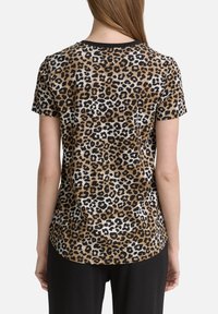 T-shirt à imprimé léopard en brun clair, noir et blanc. Manches courtes, col rond, le tissu semble doux avec un léger stretch.