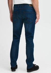 Jeans de mezclilla azul oscuro con un corte ajustado, que cuentan con dos bolsillos traseros y costuras en contraste. Sin logotipos ni patrones visibles.