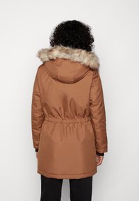 Brun polstret parka med imiteret pelskant på hætten, elastisk talje og lange ærmer, med en glat, mat finish.