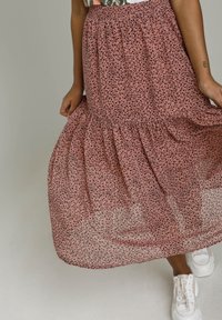 Falda rosa en capas de tela transparente con estampado de leopardo negro. Cintura elástica; combinada con zapatillas blancas. Primer plano de la textura de la tela visible.
