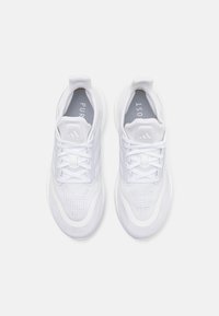 Zapatillas deportivas blancas con un perfil bajo, parte superior de malla transpirable, cierre con cordones y suela texturizada con un logotipo sutil en el talón.