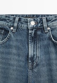 Tmavě modré džíny z denimu s klasickým designem pěti kapes, které mají stříbrný knoflíkový zapínání a kontrastní šití na švech.