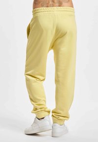 Gelbe Sweatpants mit lockerem Sitz, elastischem Bund und strukturiertem Stoff. Kombiniert mit weißen Sneakers vor einem schlichten Hintergrund.